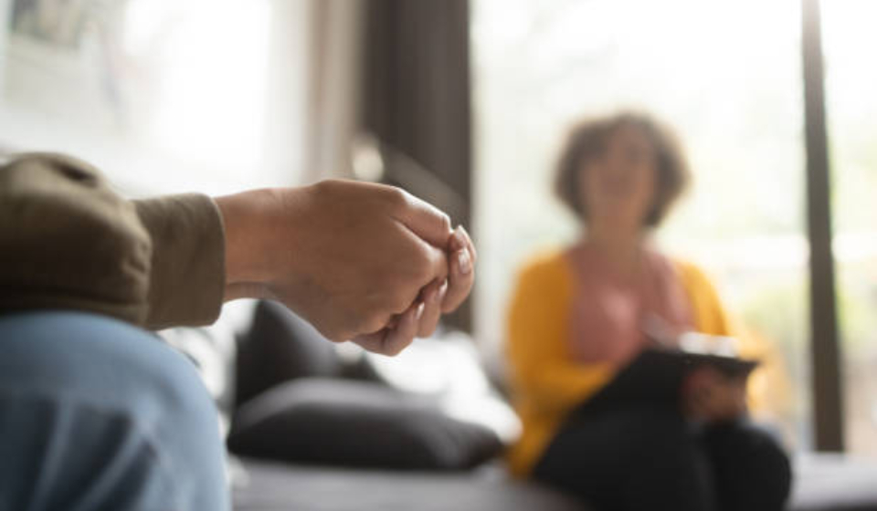 Close-up photo of a teenage girl's hands with fingers crossed nervously. She is in a therapy session with her psychotherapist.